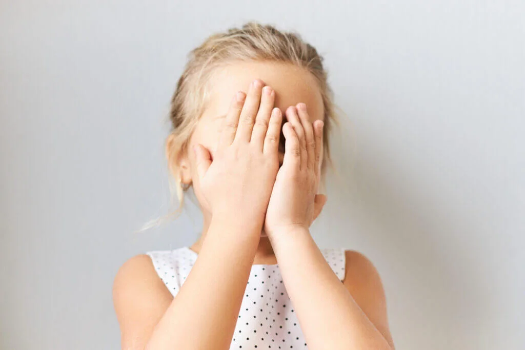 Shy timid little girl covering face, feeling scared. Embarrassed female kid posing isolated with hands on her eyes, crying, feeling ashamed because mother telling her off. Baby playing hide and seek